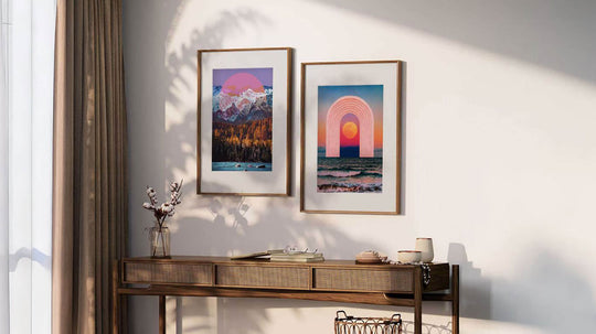 2 collage art prints, by artist Sophie Zurybida, in wooden frames with a thick white window frame, hung on a wall above a console table.