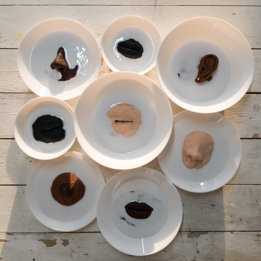 A series of varying sized white ceramic dishes, each with different fetishised black womens face and bodily features emerging from the bottom of the dish.