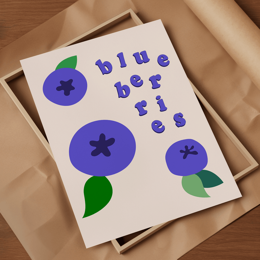 Art print of cartoon colour block purpley blue blueberries with green leaves and blue text saying ‘blueberries’ in floating letters. The print is resting on a light wooden frame on top of brown parcel paper.