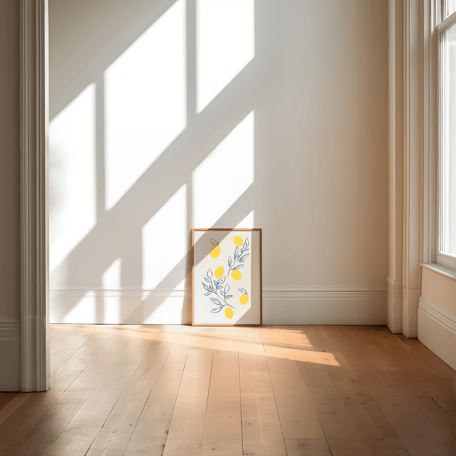 
Art print of lemons in block yellow and wispy navy blue leaves and stems scattered on an off white page. Print is in a wooden frame, on a wooden floor, leaning against a white wall.