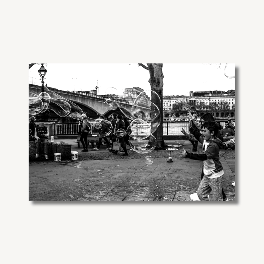 Black and white, high contrast photograph of some children chasing bubbles, near the Thames in central London.