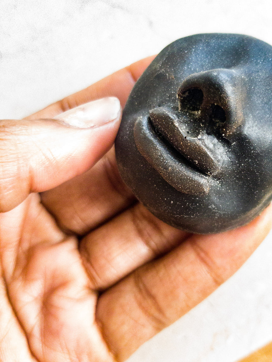 Close up of black woman’s hand holding a small iron/black stone coloured resin cast sculpture of a face with no eyes.