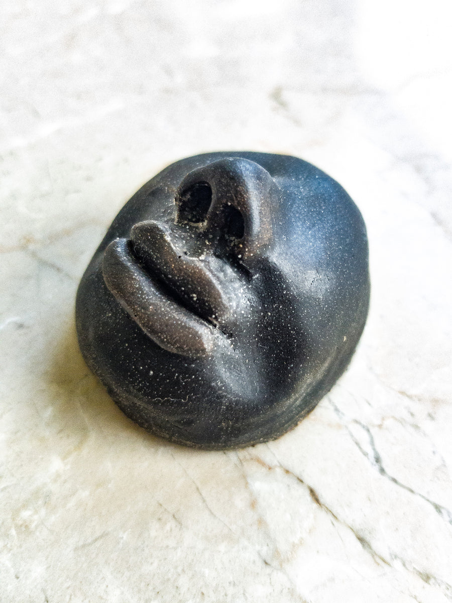 Iron/black stone coloured resin cast sculpture of a face with no eyes, with a focus on the large lips and nose, highlighting traditionally ‘black’ facial features.