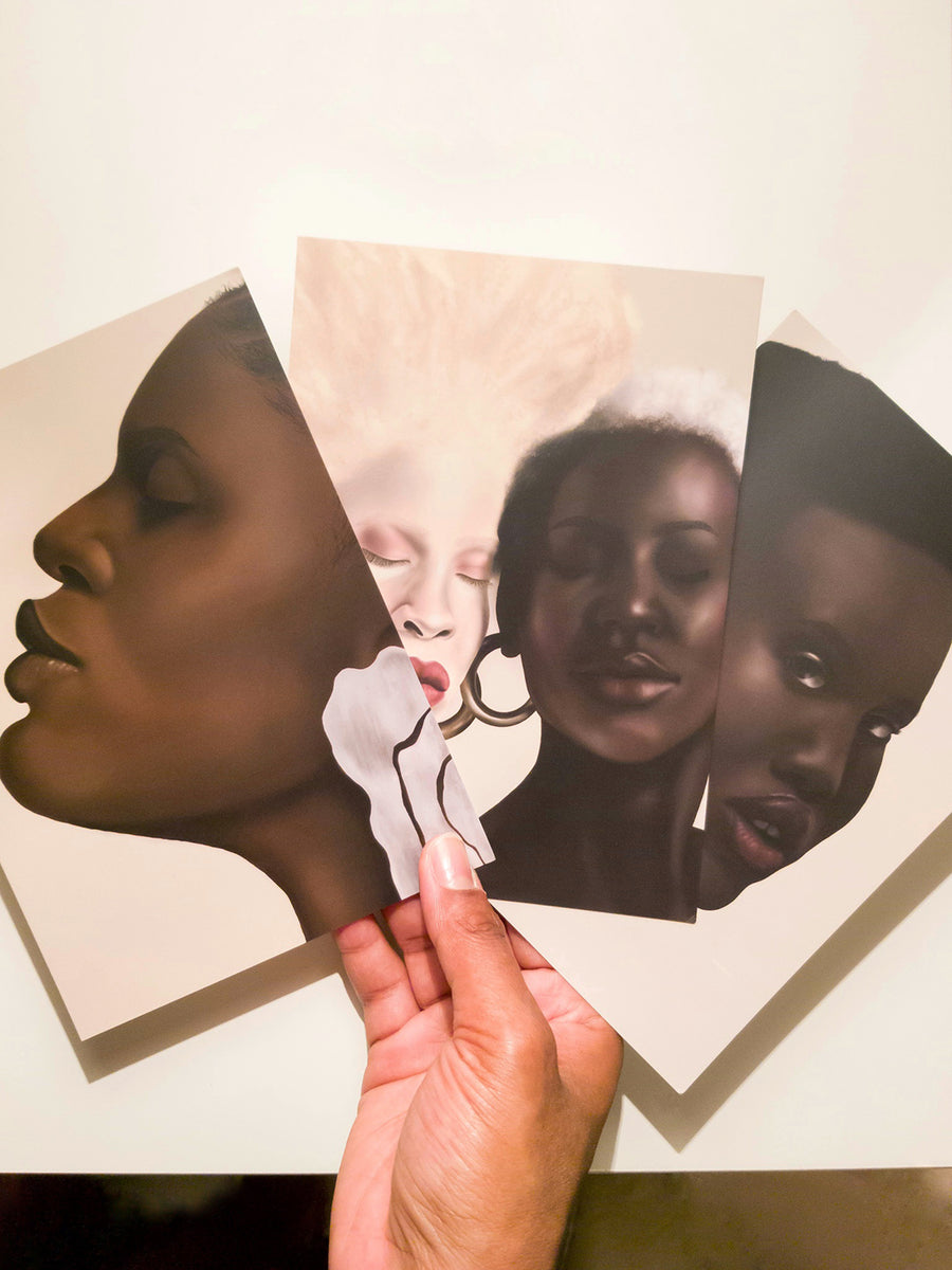 Lauren-Marie's hand holding 3 of her prints - 'Hold your head up', 'Pigment' and 'Pigment (cont.).  3 art prints of digital paintings of beautiful black women with different hair styles and skin tones.