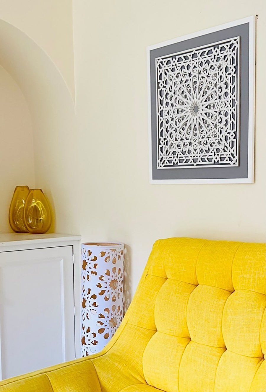 White, Islamic pattern, laser cut artwork on wall in a living room, surrounded by a yellow chair, yellow vases.