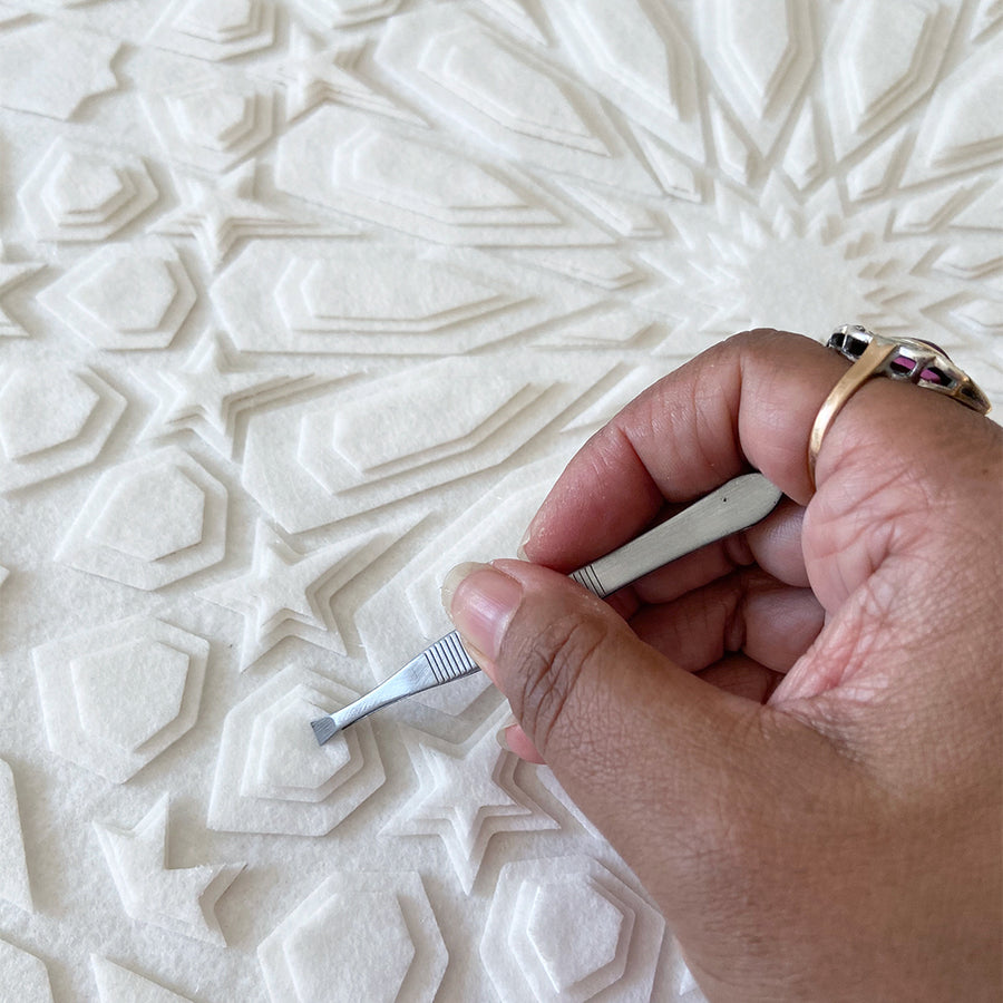 Close up showing artist, Jennifa Chowdhury, layering laser cut fabric pieces to create a beautiful, white artwork with intricate, Islamic geometric design.