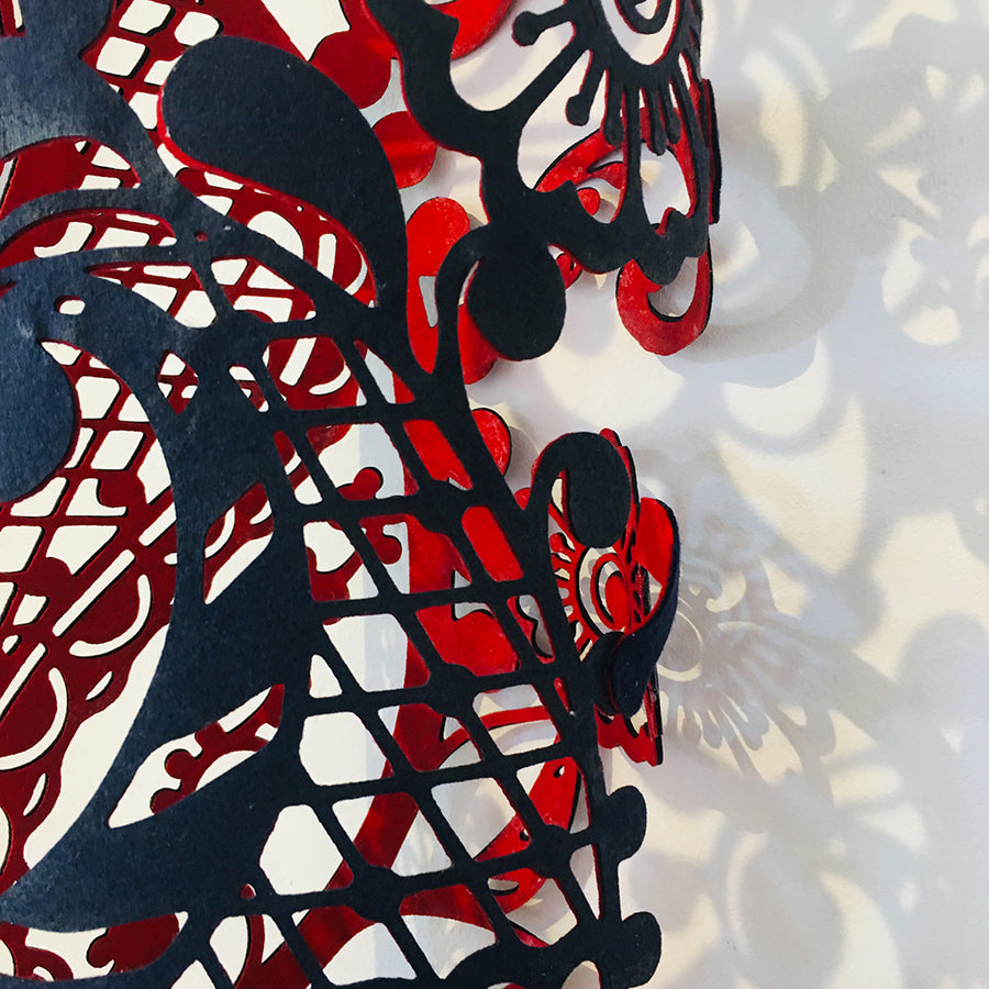 A close up showing the detailed design on this navy and red textile sculpture by Jennifa Chowdhury, inspired by traditional ‘Alta’, ‘Bindi’ and ‘Khol’ art.
