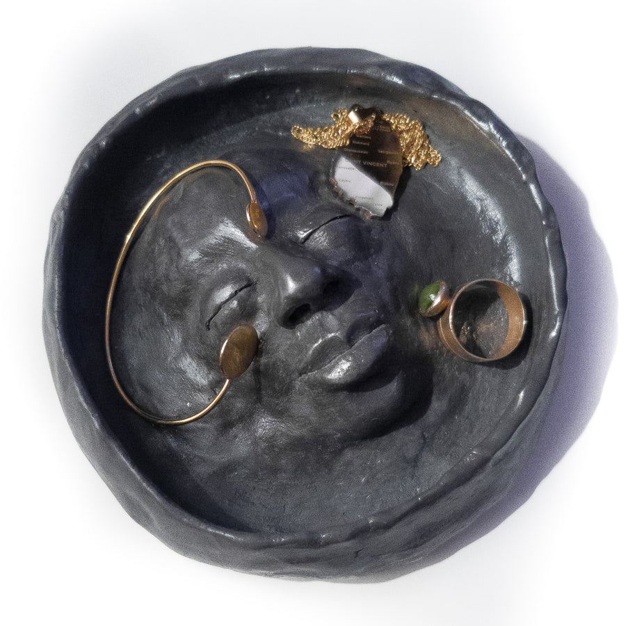 Black trinket bowl with a feminine face sculpted into the centre with jewellery inside to show how it would be used.
